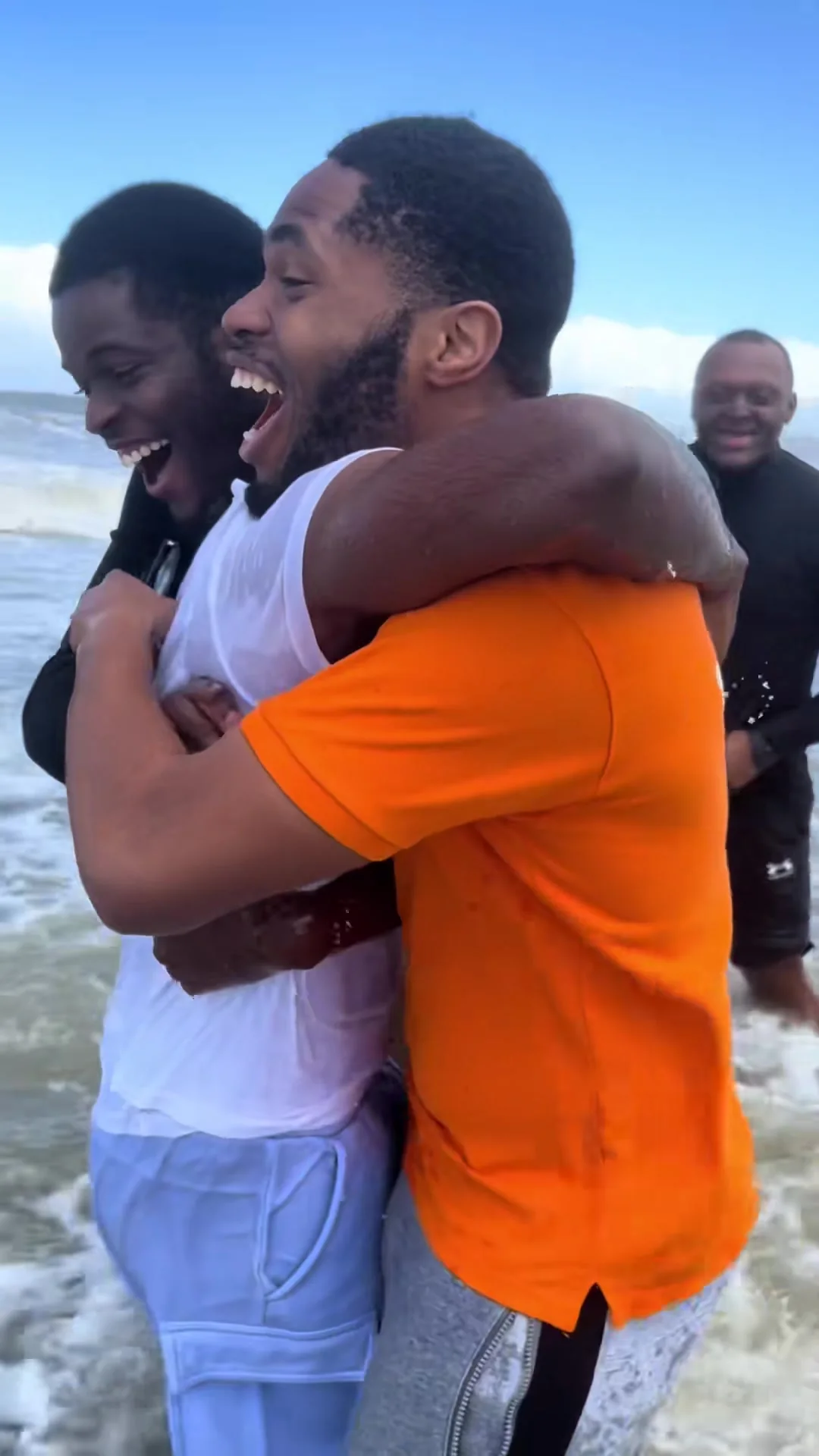 Two young men embracing and laughing in the North Sea surf after a baptism.